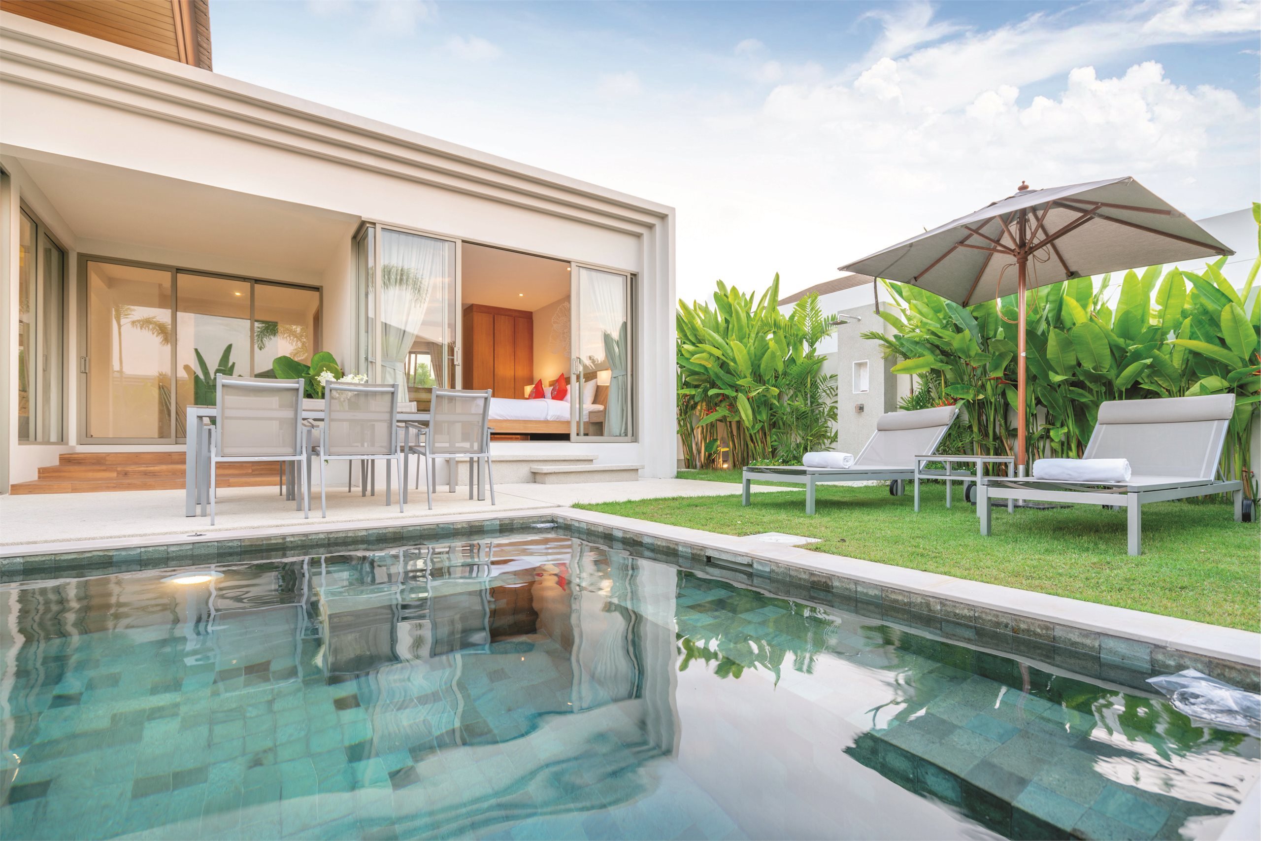 A tranquil pool beside a light-filled home and tropical garden